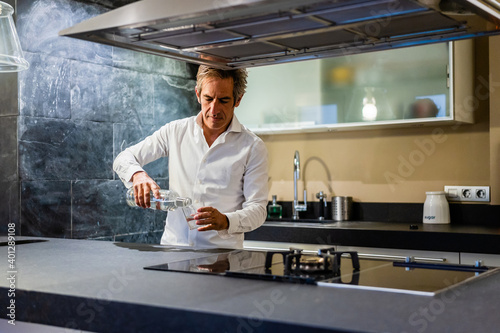 Thoughtful professional chef preparing dish while filling glass with water in modern kitchen photo