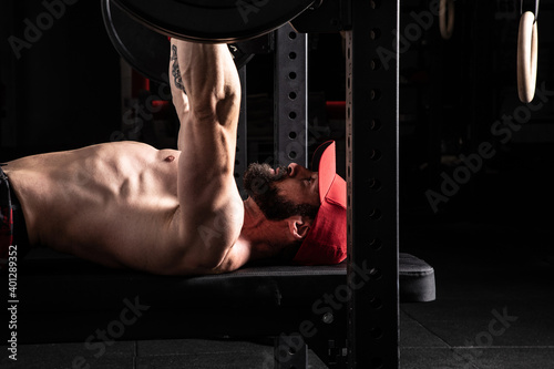 Side view of strong focused male athlete lying on bench press and doing exercises with heavy barbell during workout in gym