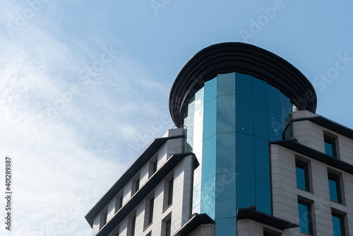 Facade of contemporary building with glass tower and windows reflecting blue sky on sunny day in city