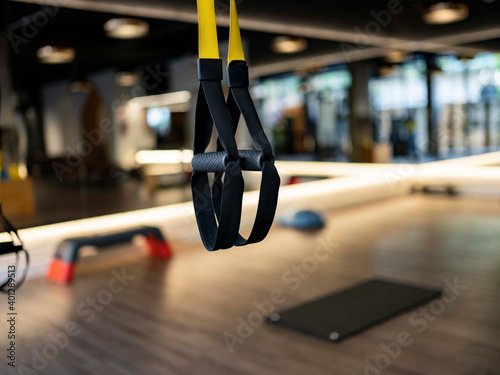 Elastic TRX ropes hanging on blurred background of contemporary gym during fitness workout