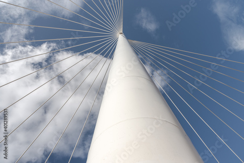 From below of white contemporary suspension bridge with high column connecting many cables together against blue sky