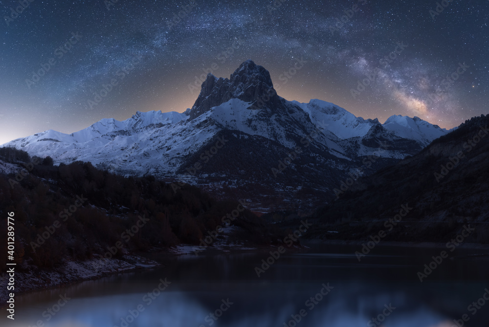 Scenery view of glowing starry dark sky above snowy mounts and pond at dusk during milky way phenomenon