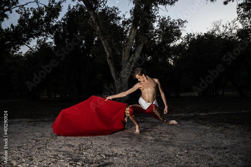 Side view of slender male bullfighter in red costume and with vivid cloak performing alone in nature in evening photo
