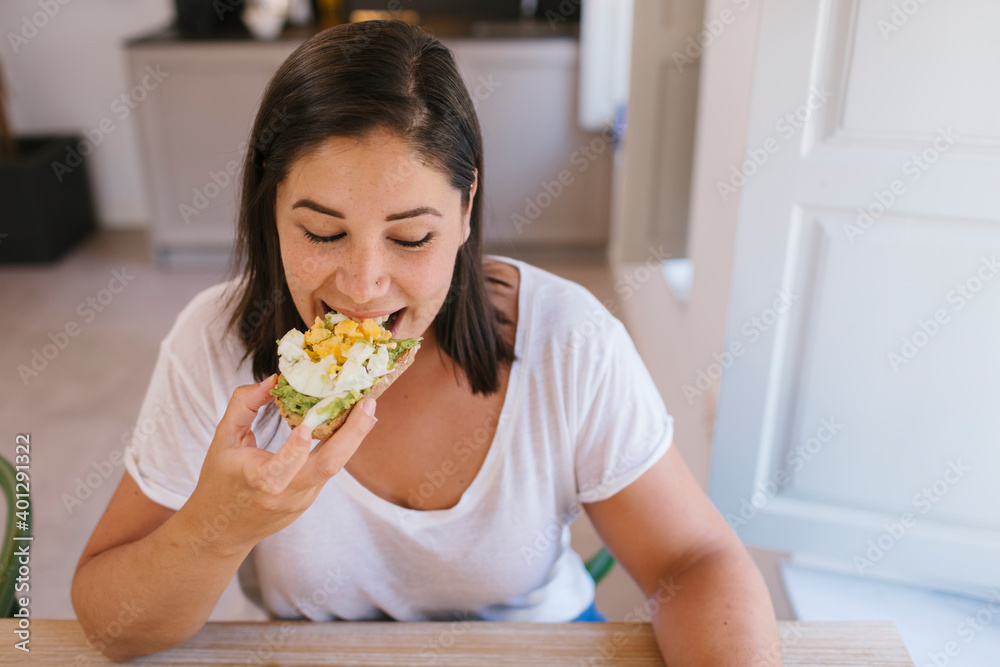 Woman biting a breakfast toast of avocados and eggs Woman biting a breakfast toast of avocados and eggs