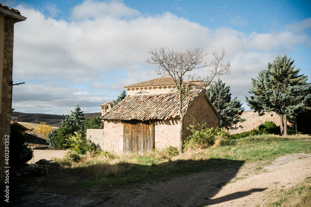 Weathered stone building with shabby tiled roof and dried leafless tree growing nearby in village located on hilly terrain with green trees in sunny autumn day with blue cloudy sky Weathered stone building with shabby tiled roof and dried leafless tree growing nearby in village located on hilly terrain with green trees in sunny autumn day with blue cloudy sky