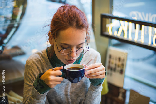 High angle of stylish female sitting at table in cozy cafe and drinking aromatic hot beverage at weekend