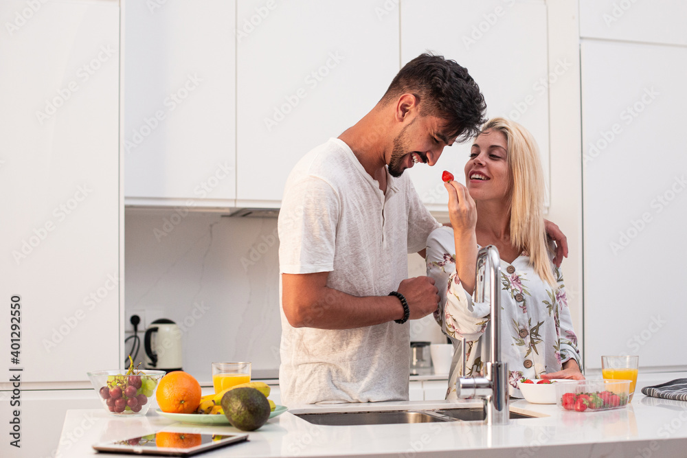 Tender couple eating strawberries and drinking fresh orange juice while hugging in kitchen in morning during breakfast