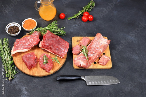 Fresh beef and pork steak with ingredients for cooking on the old table, raw meat with rosemary, pepper, tomatoes on a cutting wooden board, cooking, top view, place for text