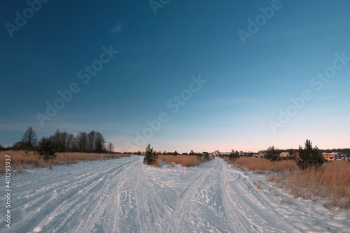 Winter, blue sky, field. The snowy road goes into the distance, in the background of the house.