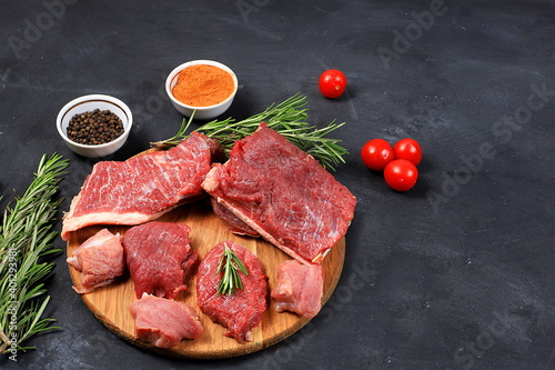 Fresh beef steak with ingredients for cooking on an old table, raw meat with rosemary, pepper, tomatoes, for grilling or skillet, cooking, top view, place for text