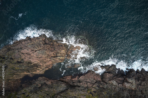 Drone view of foamy blue sea waving on rocky shoreline with rough boulders photo