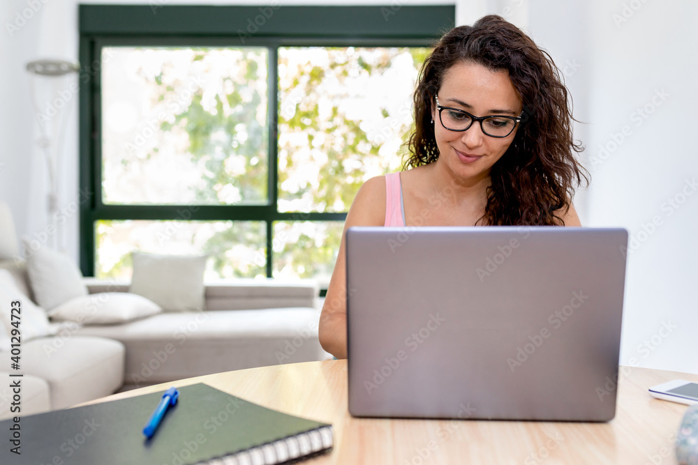 Positive young female student in casual clothes and eyeglasses sitting at table with laptop during online studies at home Positive young female student in casual clothes and eyeglasses sitting at table with laptop during online studies at home