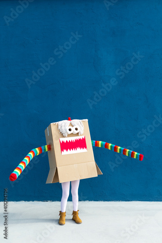 Unrecognizable playful kid wearing funny costume of monster made of carton box standing on street during holiday celebration photo