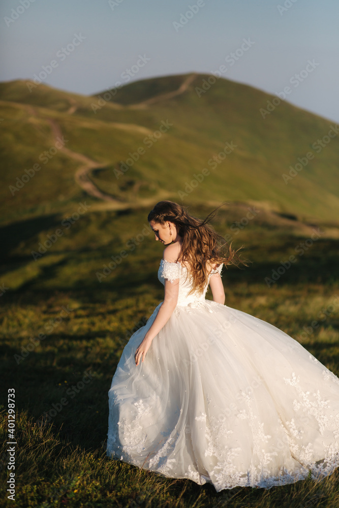 Beautiful young bride stand on the hill in mountais. Windy outdoor. Green hills on background