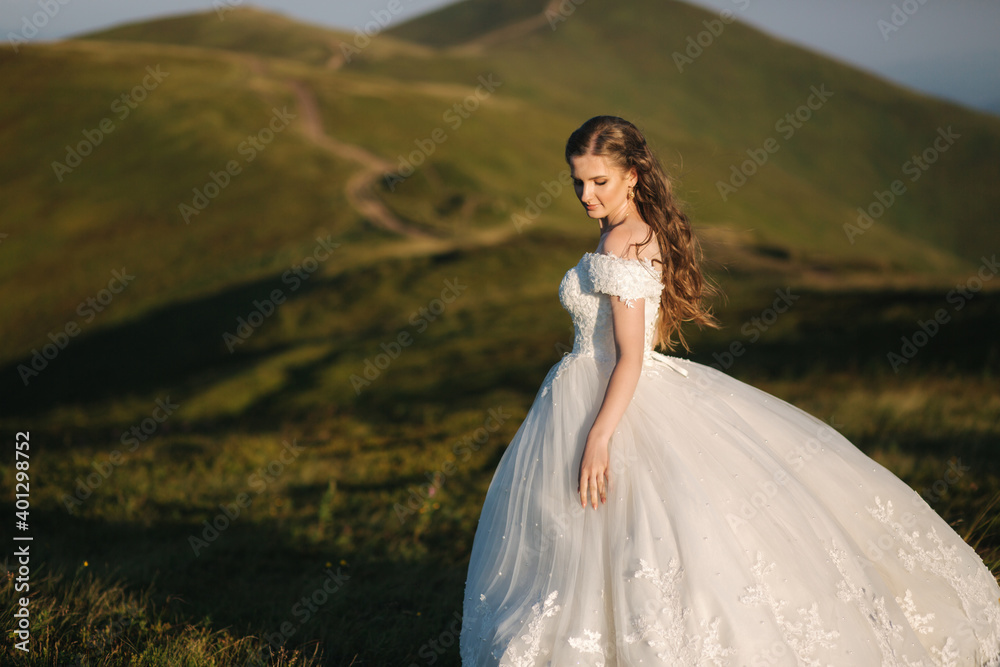 Beautiful young bride stand on the hill in mountais. Windy outdoor. Green hills on background