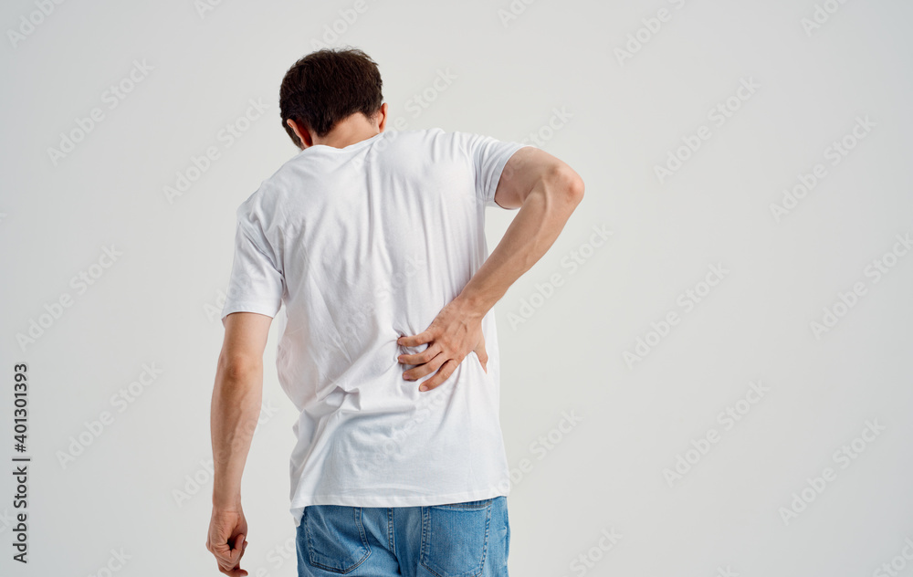 a man in a white t-shirt touches his back with his hand spine pain a man in a white t-shirt touches his back with his hand spine pain