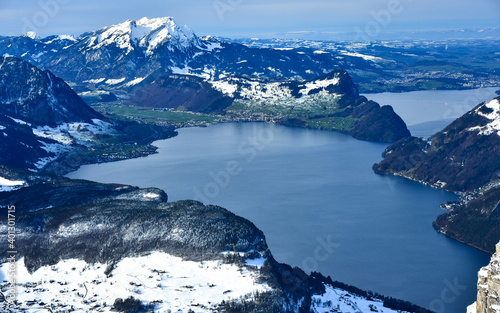 Winter scenery in Swiss Alps. Top view of a lake from the highest point in Stoos Ski Resort. The snowed, rocky, sharp, steep peaks surround the blue waters.