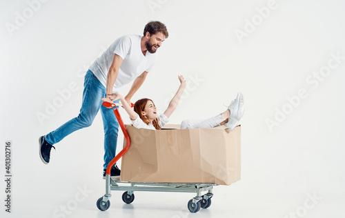 man carries a woman in a box on a cargo trolley light background fun friends