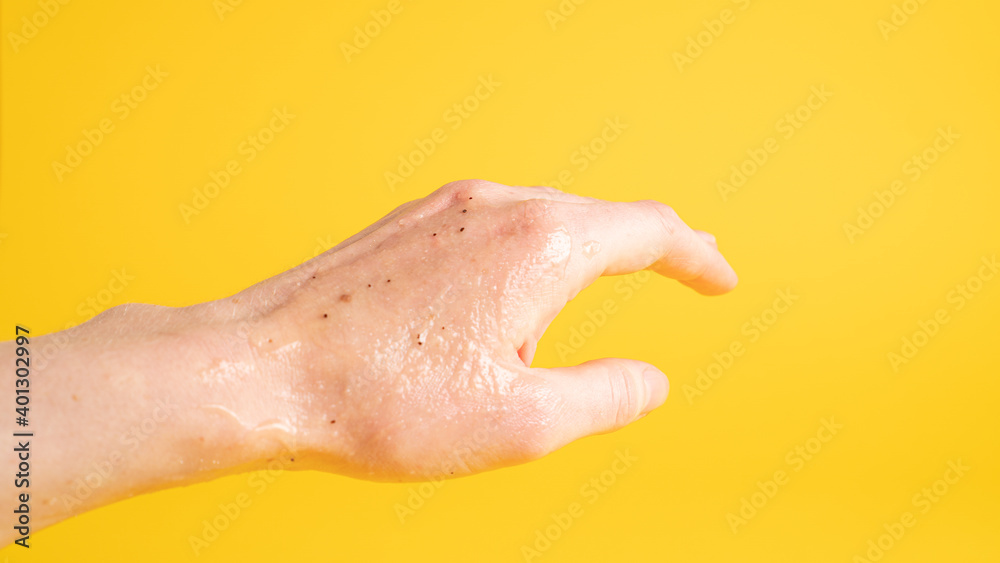 Fototapeta premium Left hand with scrub peeling gel that has black dots on yellow background