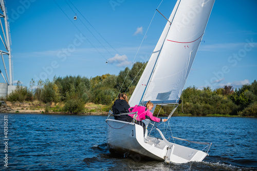 A young sailing instructor conducts a class with two female novices on a river with a beautiful landscape