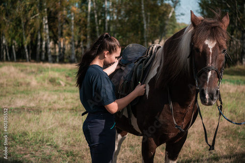 The process of saddling a horse is demonstrated by a young instructor a girl in equestrian sports. © Anna Kosolapova