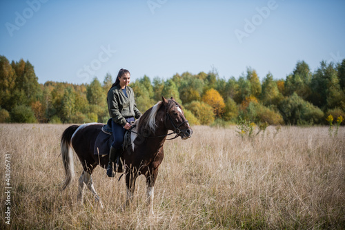 A pretty girl came to the country equestrian club and rides a horse through the fields in the fall.