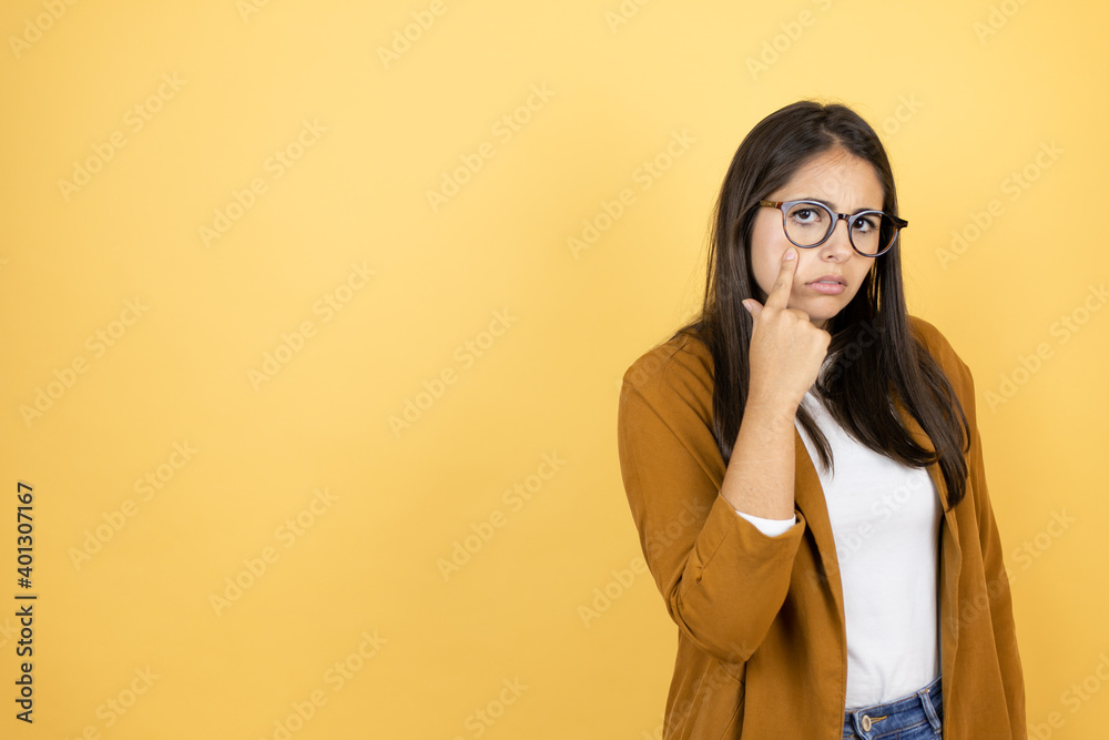 Young beautiful woman wearing a blazer over isolated yellow background Pointing to the eye watching you gesture, suspicious expression Young beautiful woman wearing a blazer over isolated yellow background Pointing to the eye watching you gesture, suspicious expression