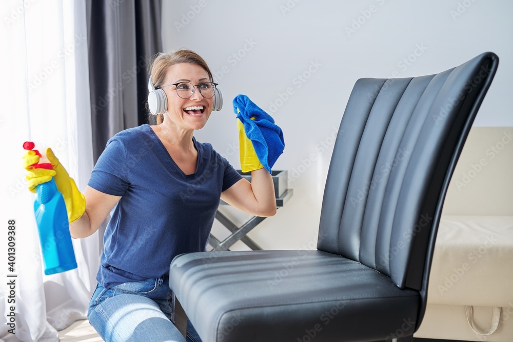 Home cleaning on positive, woman in headphones and gloves cleans armchair, furniture Home cleaning on positive, woman in headphones and gloves cleans armchair, furniture