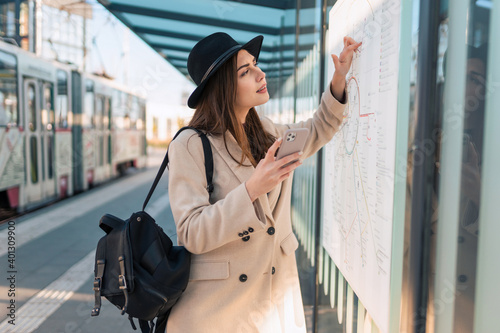 Woman tourist with phone in hand at bus stop looking on map of public transport routes © Andrii 