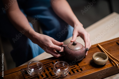 The girl is holding a ceramic teapot. Close-up of a table for a ritual tea party in China. Bamboo table with tray and cups
