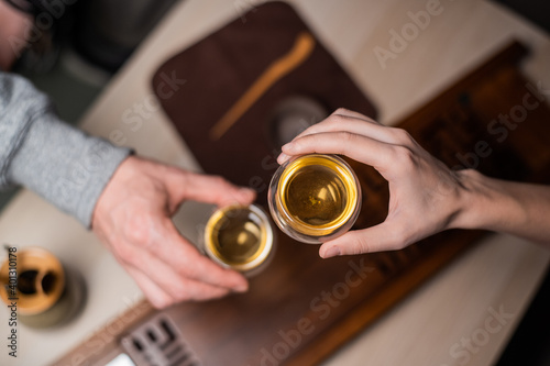 Top view of a bamboo board with a tray. Men s and women s hands close-up holding glass cups with amber tea at an intimate tea ceremony