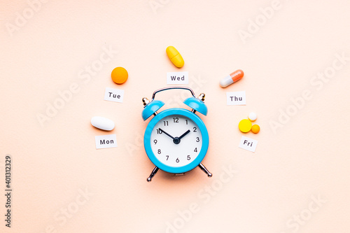 medicine drugs daily and weekly schedule concept. assorted drugs near alarm clock. above view. drug medication reminder conceptual. pink background