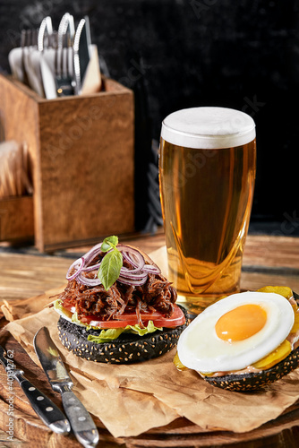 Set of hamburger with egg and beer. A standard set of drinks and food in the pub, beer and snacks. Dark background, fast food. Traditional american food.