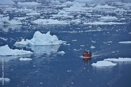 A red fishing boat passes icebergs in Disko Bay as it returns to port at Ilulissat, Greenland. photo