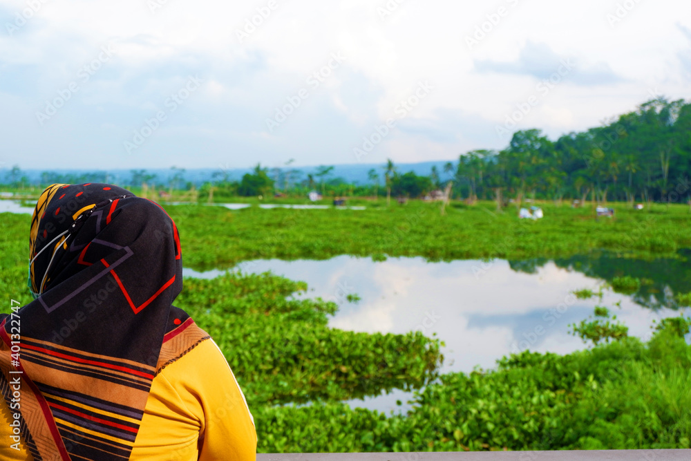 Hijab woman enjoys the river and mountain view from the bridge. Hijab woman enjoys the river and mountain view from the bridge.