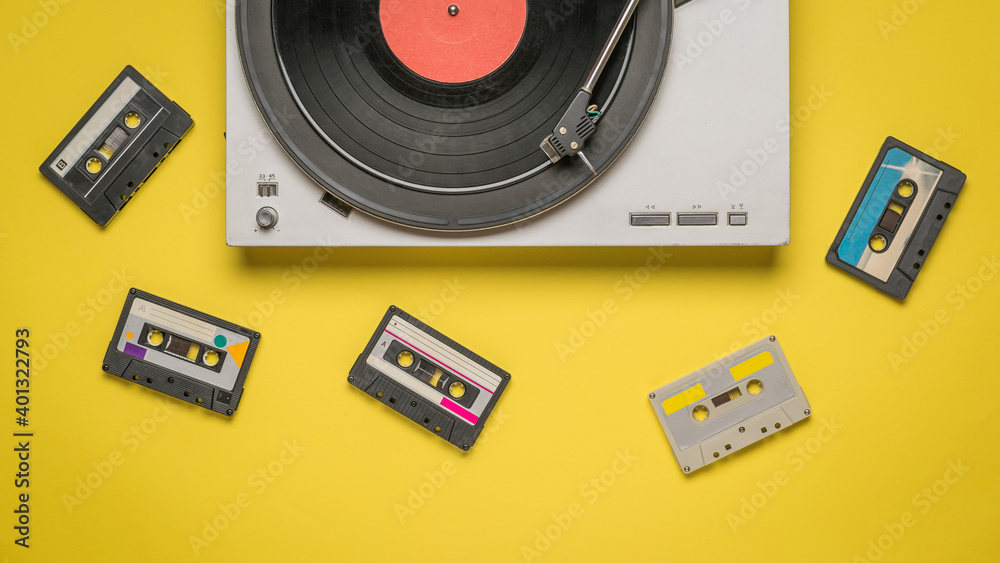 Fototapeta premium Scattered tape cassettes and a record player on a yellow background.