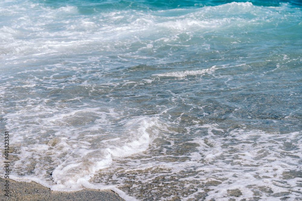 Fototapeta premium White foamy waves on sandy beach closeup. Seaside on sunny summer day. Summer vacation time concept.