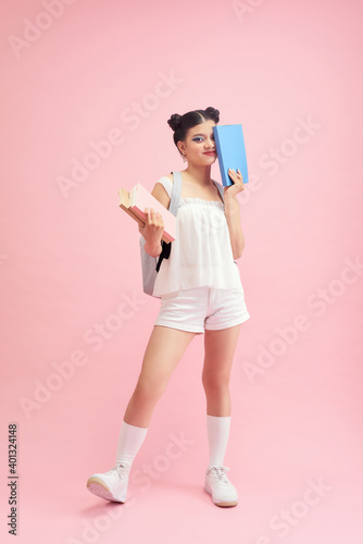 Portrait of student girl with backpack and books on pink background