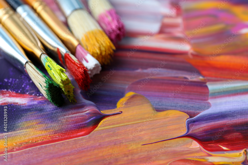 Fototapeta premium Set of different brushes on abstract colorful paint, closeup