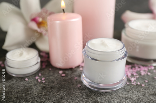 Beautiful spa composition with cosmetic products  candle and flower on grey table  closeup