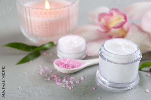 Beautiful spa composition with cosmetic products  flowers and candle on light grey table. Space for text