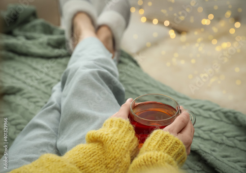 Woman with cup of tea sitting on plaid indoors, closeup