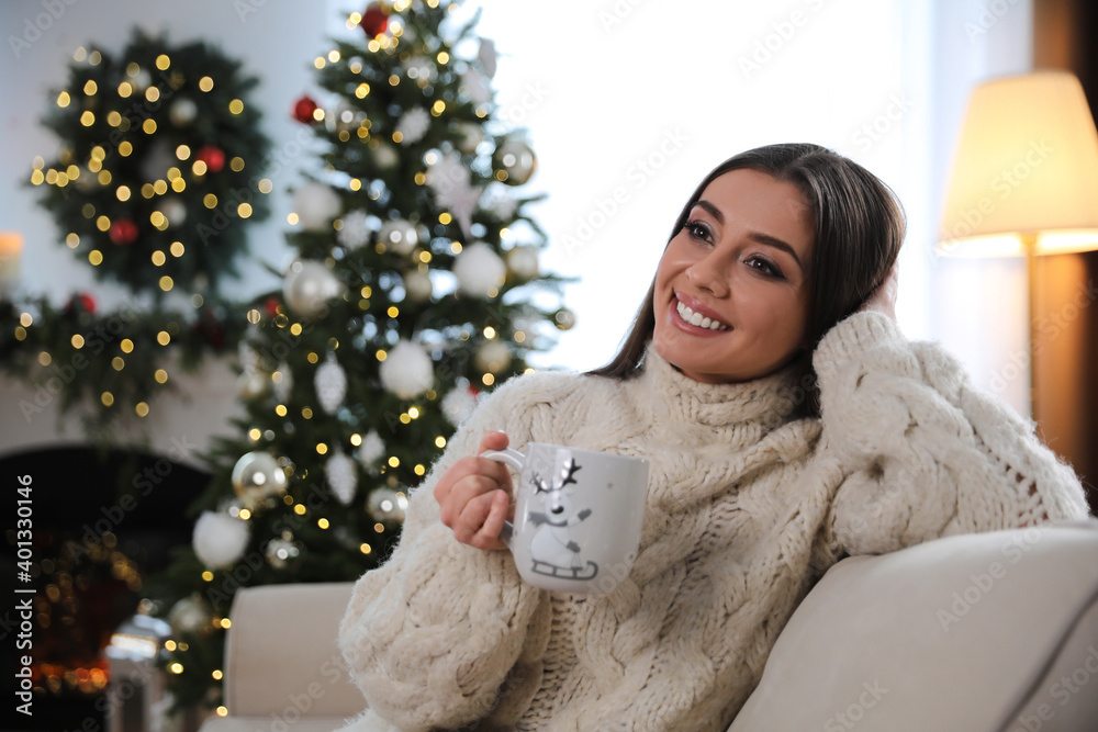 Beautiful young woman with cup of hot drink in living room decorated for Christmas Beautiful young woman with cup of hot drink in living room decorated for Christmas