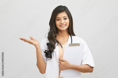 Smiling Indian female doctor greeting with clipboard against white.