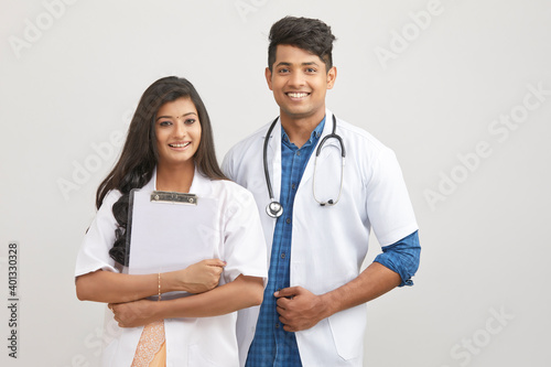 Indian young male and female doctor with note pad against white.