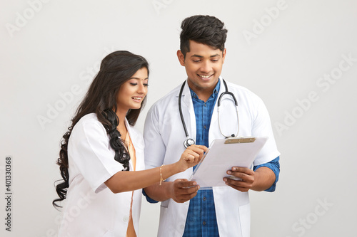 Indian young male and female doctor examining patient papers against white.