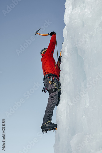 ice-climber man with ice tools axe climbing a large wall of ice. Ou