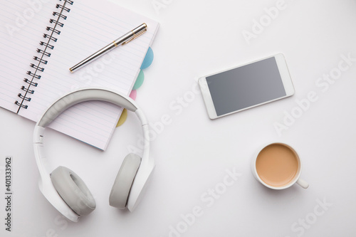 Headphone, coffee cup, smartphone with note and pen on table.