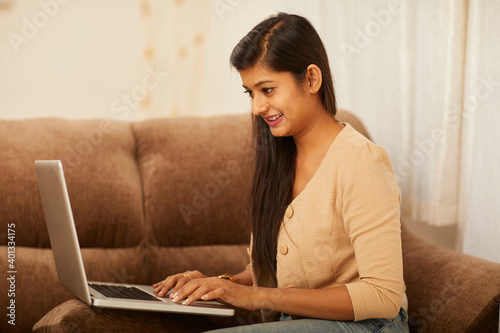 Photography Young woman working on laptop at home on sofa