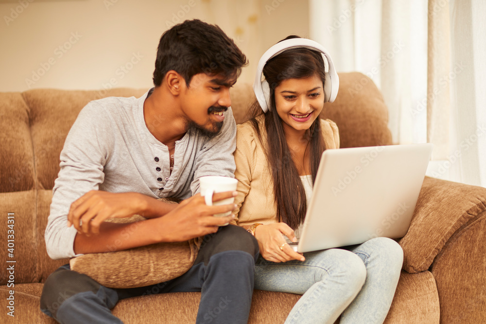 Happy young couple using laptop at home on sofa.